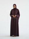 Woman wearing a dark purple abaya with a matching hijab on a white background