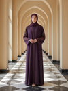 Woman in a long, dark purple dress standing in a hallway with arches.