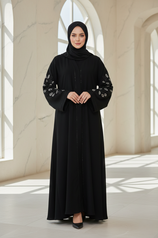 Woman wearing a black abaya with floral embroidery in a bright, sunlit room.