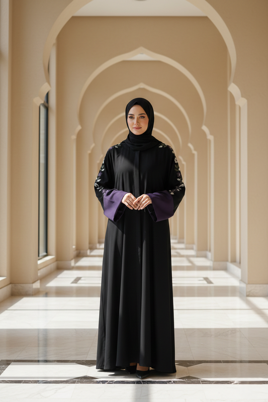Woman in a black abaya with purple cuffs standing in a hallway with arches.