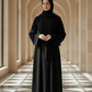 Woman in a black abaya standing in a sunlit hallway with arched ceilings.