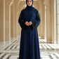 Woman in a navy blue abaya standing in a decorative hallway with arches.