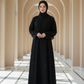 Woman in a black abaya standing in a sunlit hallway with arches.