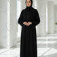 Woman in a black abaya standing in a bright, white architectural interior.