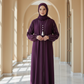 Woman in a long purple dress standing in a sunlit hallway with arches.