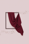Burgundy fabric draped over a black frame on a light pink background