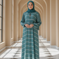 Woman in a teal dress with white stripes standing in a sunlit hallway with arches.