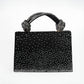 Black handbag with sparkling handle and studded design on a white background