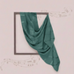 Green fabric draped over a square frame on a light pink background
